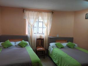 a bedroom with two beds with green pillows and a window at Hotel California in Mineral del Monte