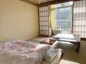 a bedroom with a bed and a table and a window at Yoshioka Ryokan in Kamogawa