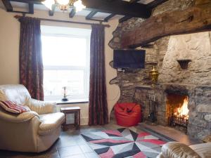 a living room with a stone fireplace and a chair at Groudd Hall Cottage in Cerrig-y-Druidion