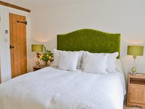 um quarto com uma cama branca com cabeceira verde e candeeiros em Priory Barn em Weald
