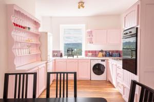 a pink kitchen with white cabinets and a dishwasher at Corner Cottage in Matlock