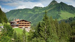 una casa en una colina frente a una montaña en Das alpine Lifestyle Berghotel Madlener, en Damüls