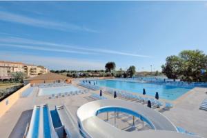 une grande piscine avec des chaises bleues et blanches dans l'établissement Bungalow dans une résidence en plein air a l'Elysée vagues océanes "capfun", au Grau-du-Roi