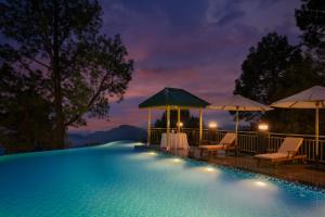 卡绍利Cassia Resort, Kasauli的游泳池在晚上提供椅子和遮阳伞