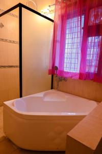 La salle de bains est pourvue d'une baignoire blanche et d'un rideau rose. dans l'établissement Hotel Wild Rose, à New Delhi