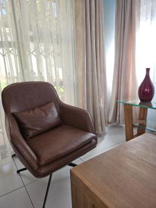 una silla marrón sentada junto a una mesa de cristal en Three Stones Executive Apartments en Maseru