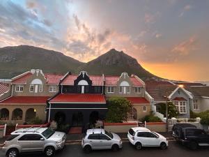 un edificio con auto parcheggiate in un parcheggio con una montagna sullo sfondo di ‘The Black Pearl’ - Surfers Corner, Muizenburg a Città del Capo