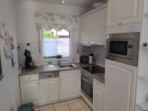 a kitchen with white cabinets and a sink and a window at Sommerhaus Nessmersiel in Neßmersiel
