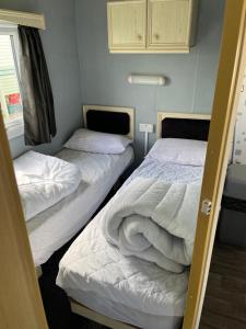 duas camas num pequeno quarto com lençóis brancos em Colemans Caravans Golden Anchor Caravan Park em Chapel Saint Leonards