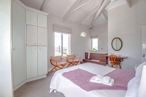 138 Marine Beachfront Guesthouse في هيرمانوس: غرفة نوم بيضاء بسرير وطاولة وكراسي