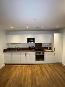 a kitchen with white cabinets and a wooden floor at Entire 2 bedroom flat in London