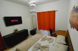 a bedroom with a bed and a tv and orange curtain at Casa Executiva Orla Morena in Campo Grande
