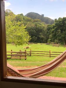 a hammock looking out a window at a field at Sitio Eco Friends - Perfeita para Casal e Família! in São Bento do Sapucaí