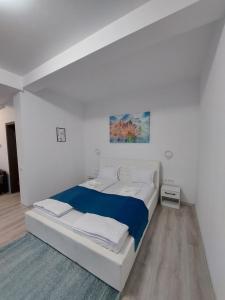 a white bedroom with a large bed with blue sheets at NoMi Ultracentral Apartments in Târgu-Mureş