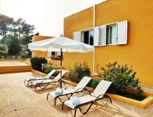 vier Stühle und ein Regenschirm vor einem Gebäude in der Unterkunft Bonita Casa con piscina privada y amplio jardin in Sant Francesc de s'Estany