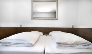 ein Bett mit zwei Kissen und einem Spiegel an der Wand in der Unterkunft Stadthotel Heilbronn in Heilbronn