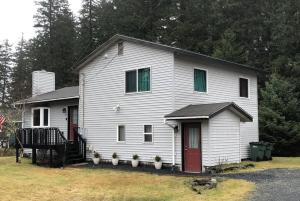 Biały dom z czerwonymi drzwiami i roślinami na podwórku w obiekcie Den Mishka - Kodiak's Den of the Little Bear w Kodiak