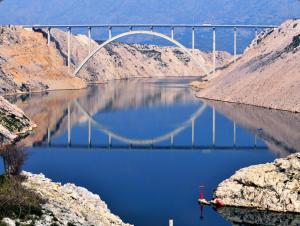 a bridge over a river with blue water at Family Hotel Zanè in Pag