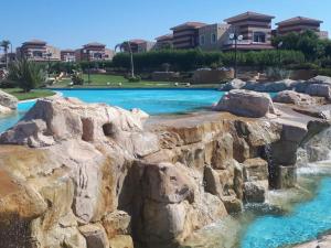 ein Pool in einem Resort mit blauem Wasser und Felsen in der Unterkunft Chalet Rosana Resort الساحل الشمالى in Dawwār al Ḩajj Aḩmad