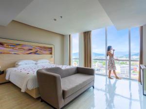 a woman walking in a hotel room with a bed and a chair at Novotel Phuket City Phokeethra in Phuket