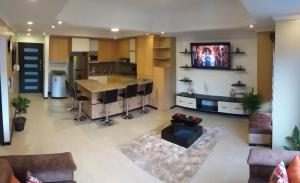 a living room with a kitchen and a tv on a wall at Departamento 2B en Condominio La Victoria in Cuenca
