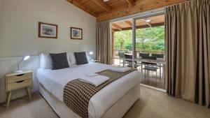a bedroom with a bed and a balcony with a table at Beechworth Cedar Cottages in Beechworth