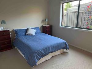 a bedroom with a bed with blue sheets and a window at Mid Coast Stayz in Waurn Ponds