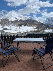 een tafel en 2 stoelen op een patio met met met sneeuw bedekte bergen bij Monolocale con terrazzo e vista spettacolare sui monti in Sestriere