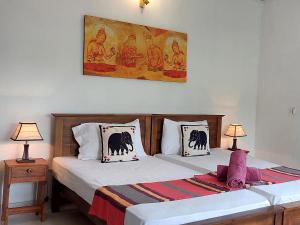2 camas en un dormitorio con 2 lámparas y una pintura en The Comfort, en Kandy