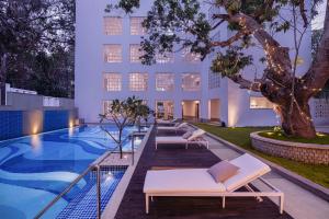 a hotel pool with lounge chairs and a tree at The Yellow House, Goa - IHCL SeleQtions in Anjuna