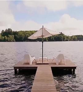 zwei Stühle und ein Regenschirm auf einem Dock auf einem See in der Unterkunft Ma Cabane Au Bord Du Lac in Neuvic