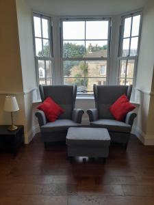 2 Stühle und ein Hocker in einem Zimmer mit Fenstern in der Unterkunft Kirkcudbright Holiday Apartments - Apartment E in Kirkcudbright