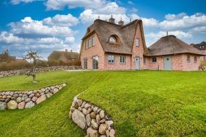 an old house with a thatched roof on a grass field at Hotel Duene in Rantum