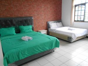 - une chambre avec 2 lits avec des draps verts et un mur en briques dans l'établissement Rumah Syariah Bugenvil, à Bandung