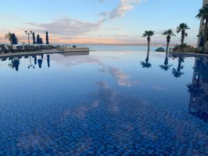 a large swimming pool with palm trees and the ocean at Samarah Dead Sea Resort Apartment with Sea View FP4 Traveler Award 2024 Winner in Sowayma