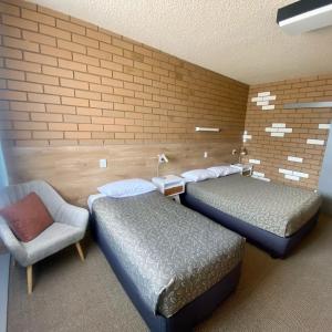 a room with two beds and a chair and a brick wall at Mount Wycheproof Motor Inn in Wycheproof