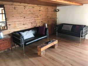 ein Wohnzimmer mit einem schwarzen Ledersofa und einer Holzwand in der Unterkunft Alphütte Riederalp Planier in der Aletsch Arena in Riederalp