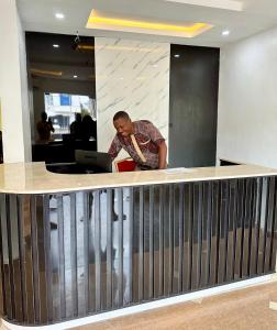 a man standing at a counter with a laptop at Whitehouse Msquare Hotel in Ikeja