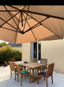 een houten tafel en stoelen onder een grote parasol bij maison de vacances ninette in Névez