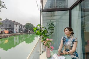 Una mujer sentada en un alféizar junto a un río. en Tongli Slowlife River View Inn en Suzhou