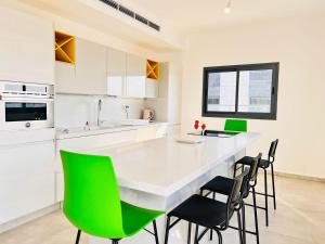 a kitchen with a white counter and green chairs at Luxury Penthouse 5 Rooms in Or Yehuda