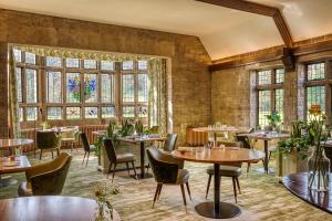 um restaurante com mesas, cadeiras e janelas em The Manor House Hotel and Golf Club em Castle Combe