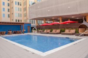 TownePlace Suites by Marriott Dallas Downtown في دالاس: مسبح فيه كراسي ومظلات على مبنى