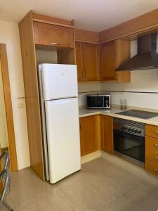 a kitchen with a white refrigerator and wooden cabinets at Apartamento San Vicente in Villar del Arzobispo