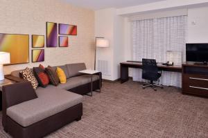 Residence Inn by Marriott East Lansing في إيست لانسنغ: غرفة معيشة مع أريكة ومكتب في غرفة الفندق