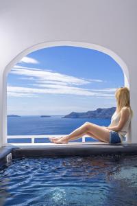 a woman sitting on the edge of a swimming pool at White Pearl Villas in Oia