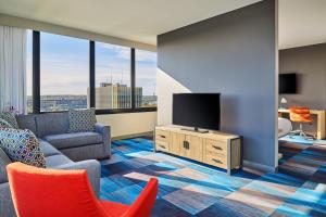 a living room with a tv and a couch and chairs at Aloft South Bend in South Bend