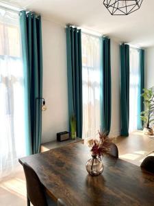 comedor con mesa de madera y cortinas verdes en Grand appartement cosy lumineux, en Saint-Maximin-la-Sainte-Baume