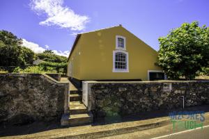 una casa amarilla detrás de una pared de piedra en Casa do Merendário, en Praia da Vitória