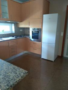 a kitchen with a white refrigerator and wooden cabinets at Casa T4 perto da Praia in Fão
